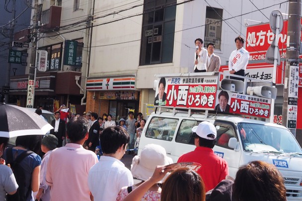 強い日差しの中、大勢の人が足を止めて演説を聞く。司会は村越祐民千葉5区総支部長。